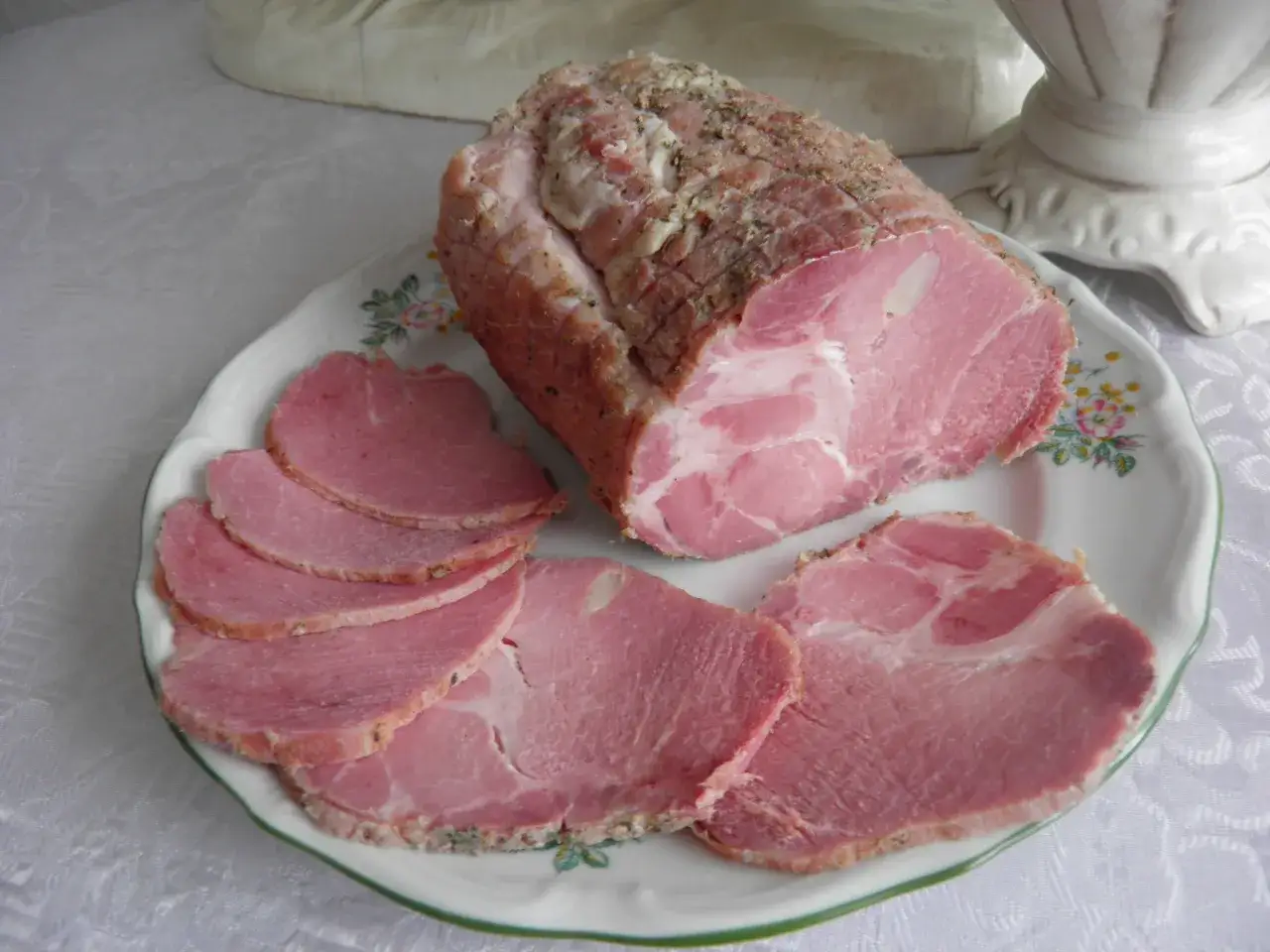 Karkówka po peklowaniu do wędzenia, pokrojona w plastry, leży na talerzu.