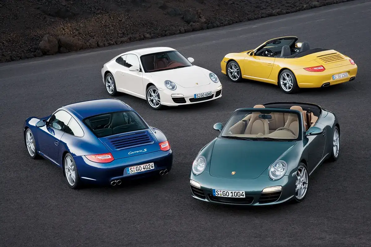 Cztery Porsche 997: niebieski coupe, biały coupe, żółty kabriolet i zielony kabriolet, stoją na drodze.