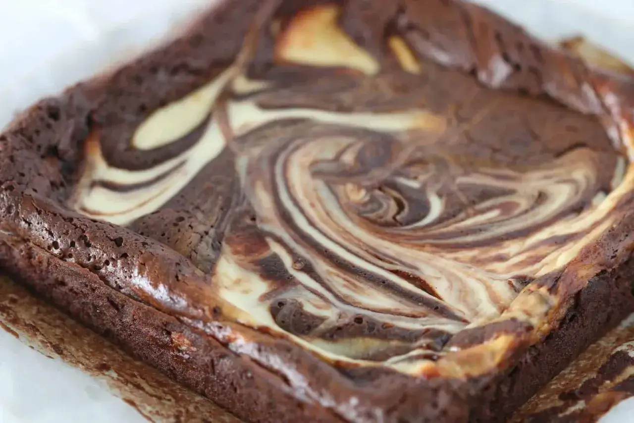 Ein Quadrat aus saftigen Cheesecake Brownies mit wirbelnden Schokoladen- und Frischkäse-Mustern.