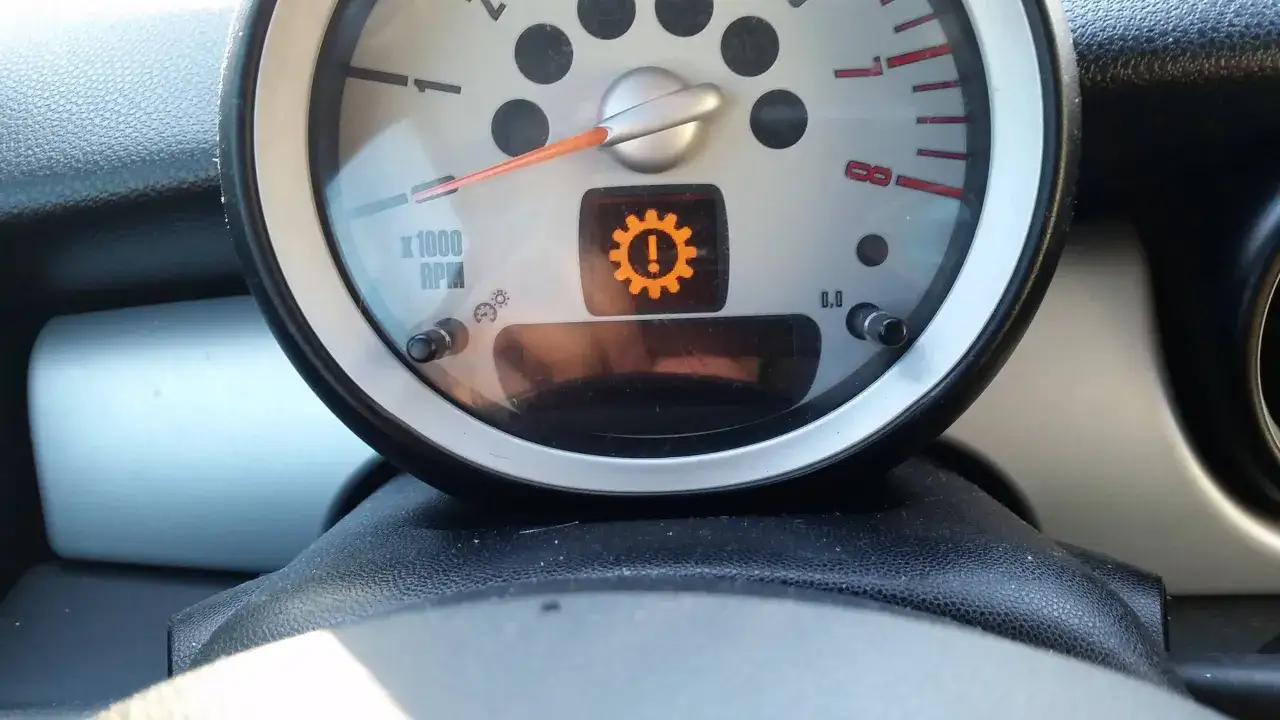 Warnleuchte im Auto: ein Zahnrad mit Ausrufezeichen. Das Getriebe-Zeichen leuchtet orange auf.