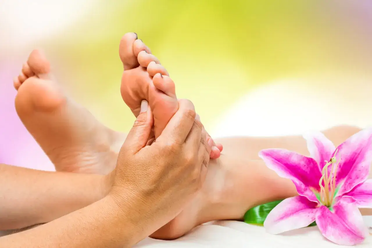 Mains massant un pied, avec une fleur de lys rose. D&eacute;couvrez les bienfaits du massage plantaire pour une relaxation profonde.