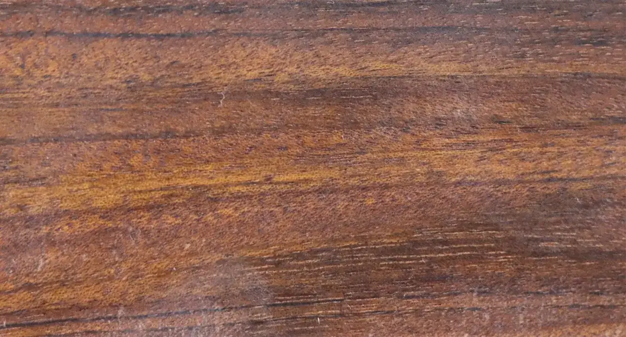 Textura rica y cálida de madera mongoy, con vetas oscuras y tonos dorados que evocan la naturaleza.