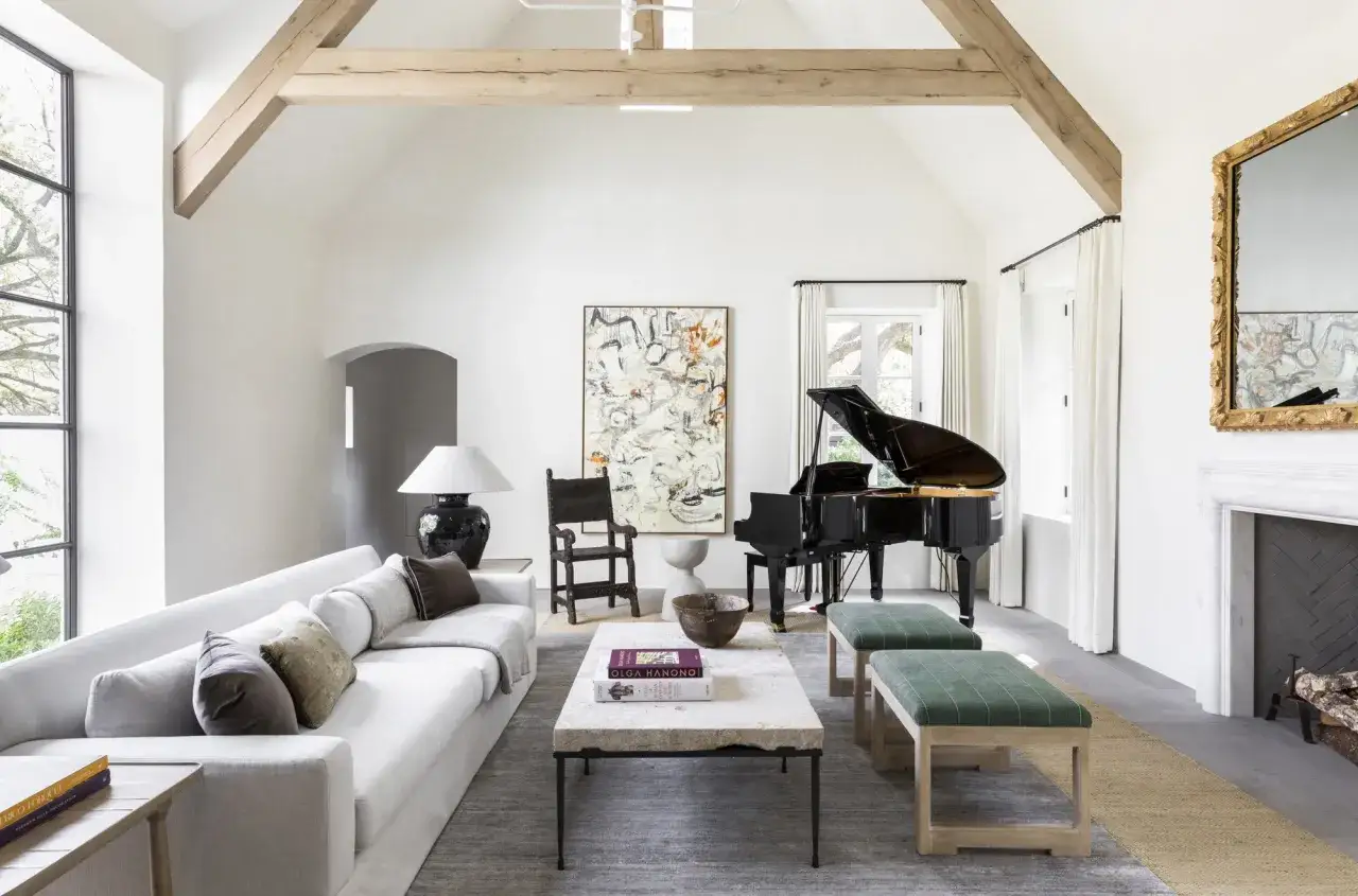 A spacious living room features multiple rugs, a grand piano, a white sectional sofa, and a large abstract painting.