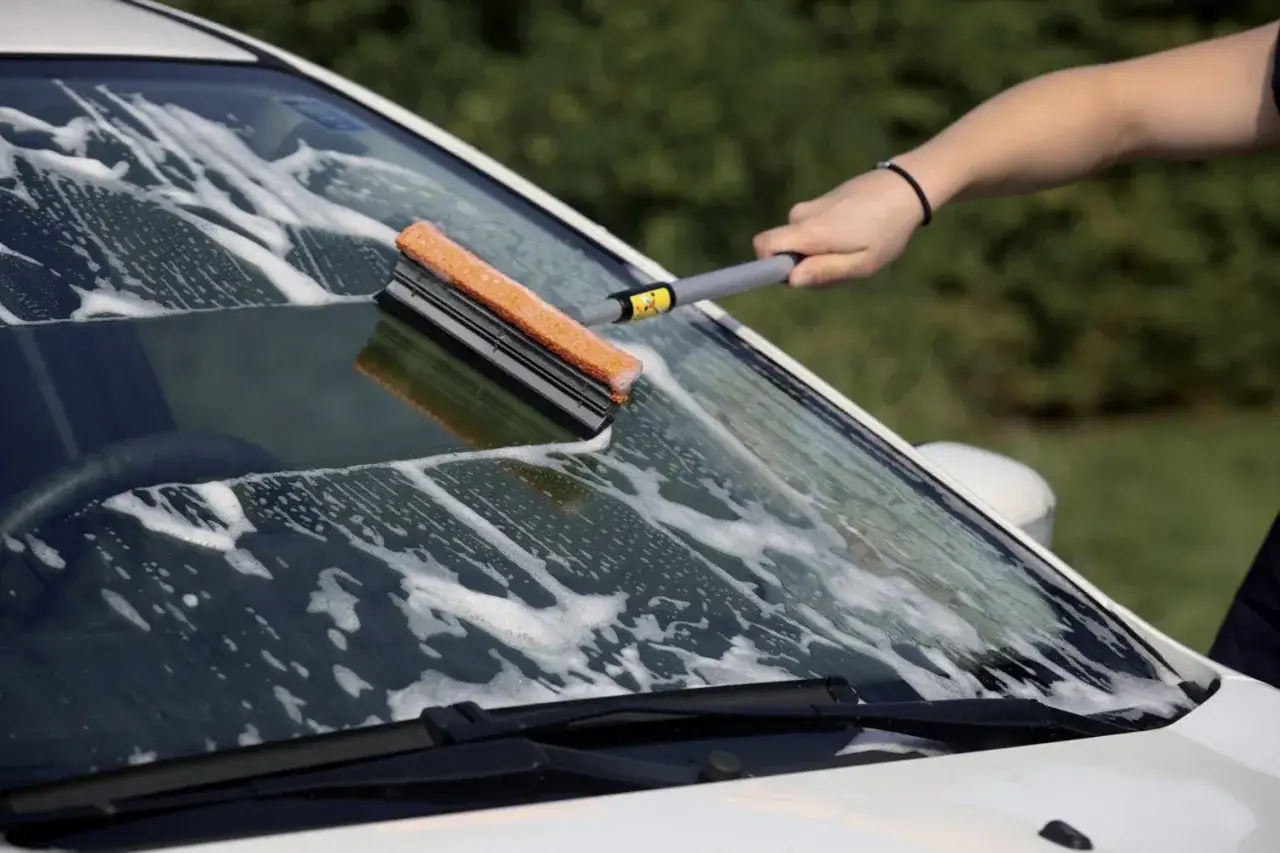 Mano che usa un attrezzo per pulire vetri dell'auto con schiuma.