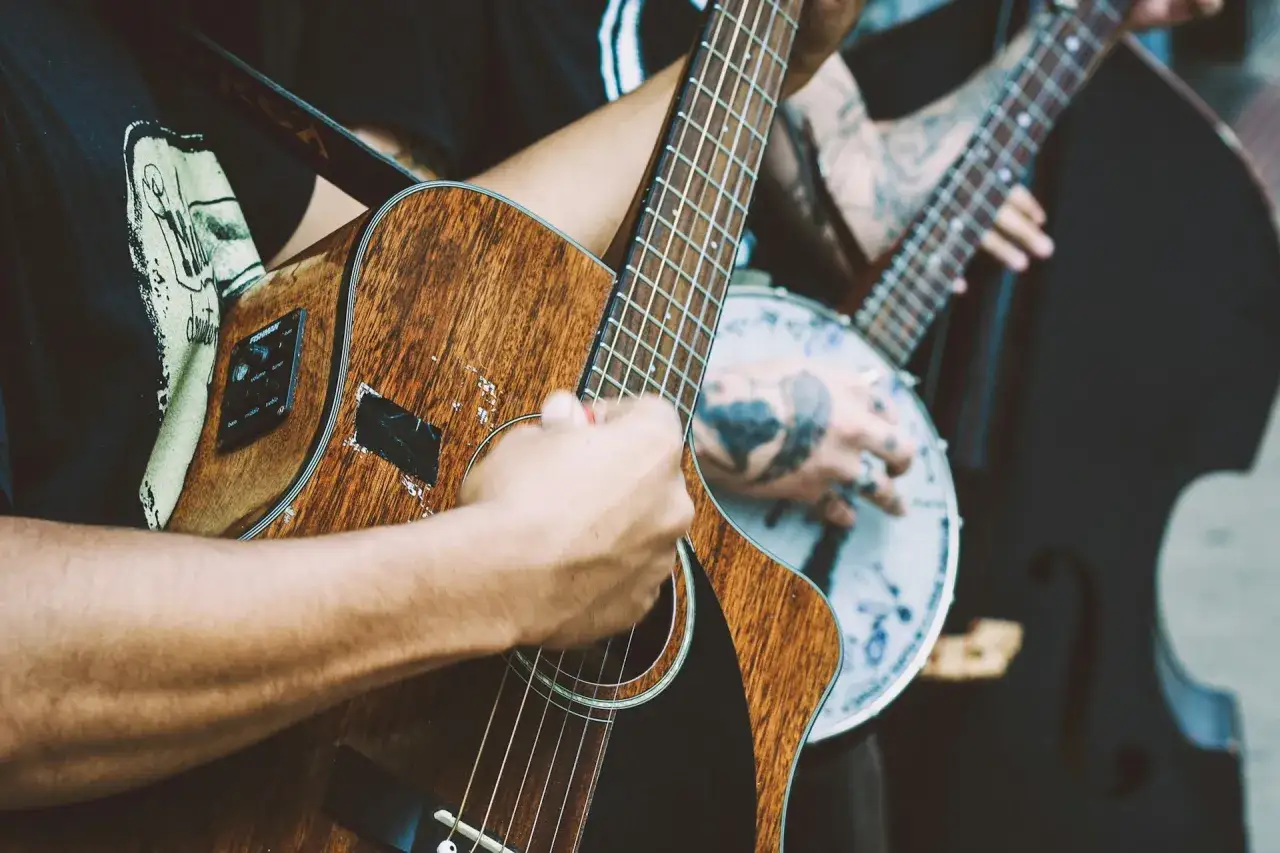 Ręce grające na gitarze, tworząc dźwięki niczym Marco Polo odkrywający nowe lądy. W tle banjo i kontrabas.