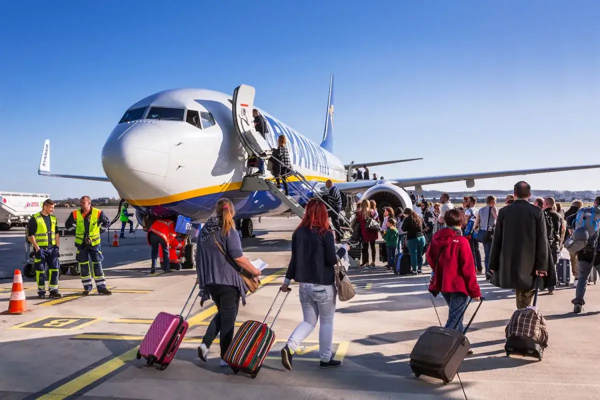 Pasażerowie z walizkami idą schodkami do samolotu Ryanair. To boarding, czyli wejście na pokład.