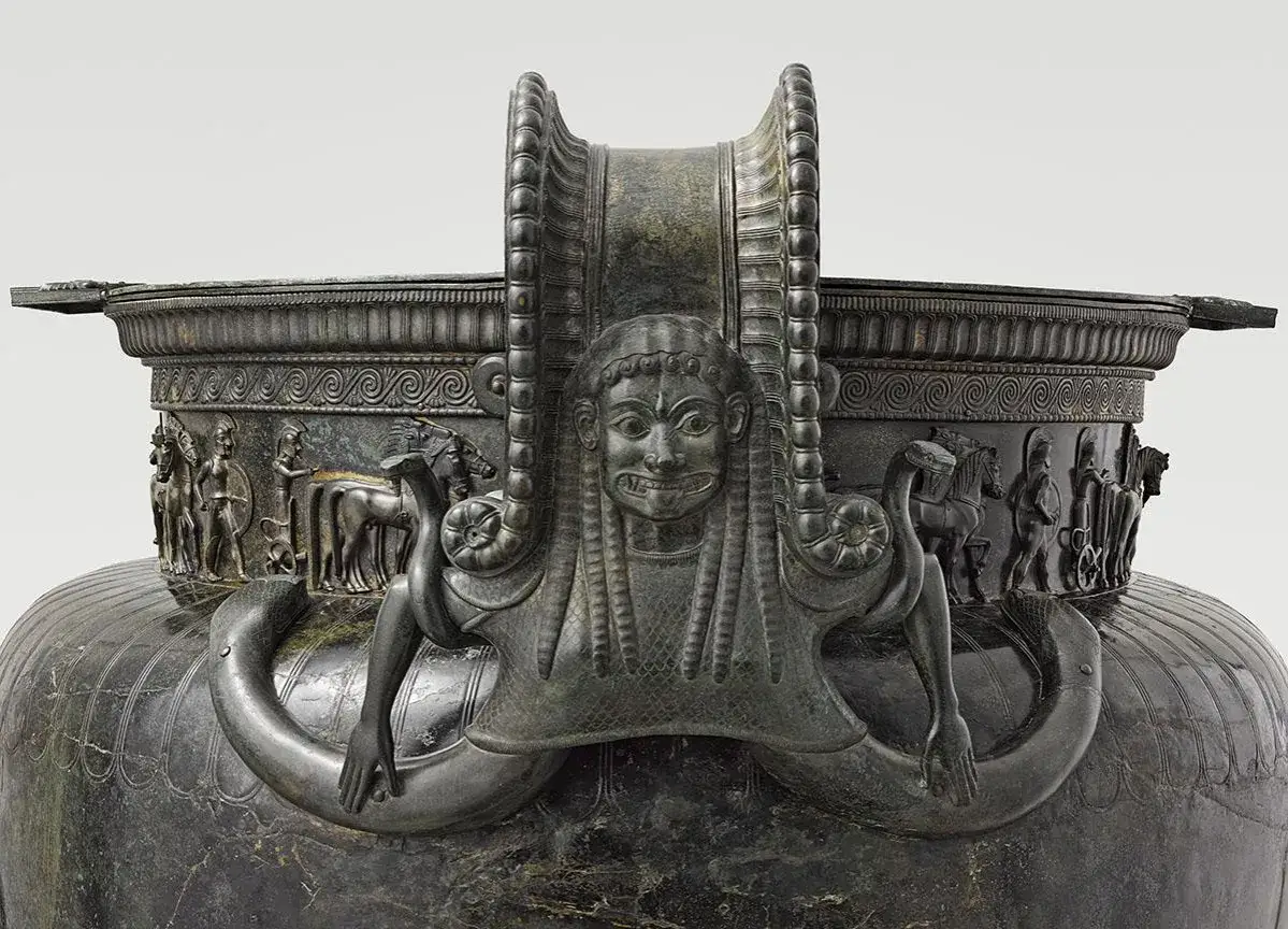 D&eacute;tail du vase de Vix : une figure f&eacute;minine aux longs cheveux, entour&eacute;e de serpents, orne la anse. Des sc&egrave;nes de procession avec des chevaux et des guerriers d&eacute;corent le pourtour.