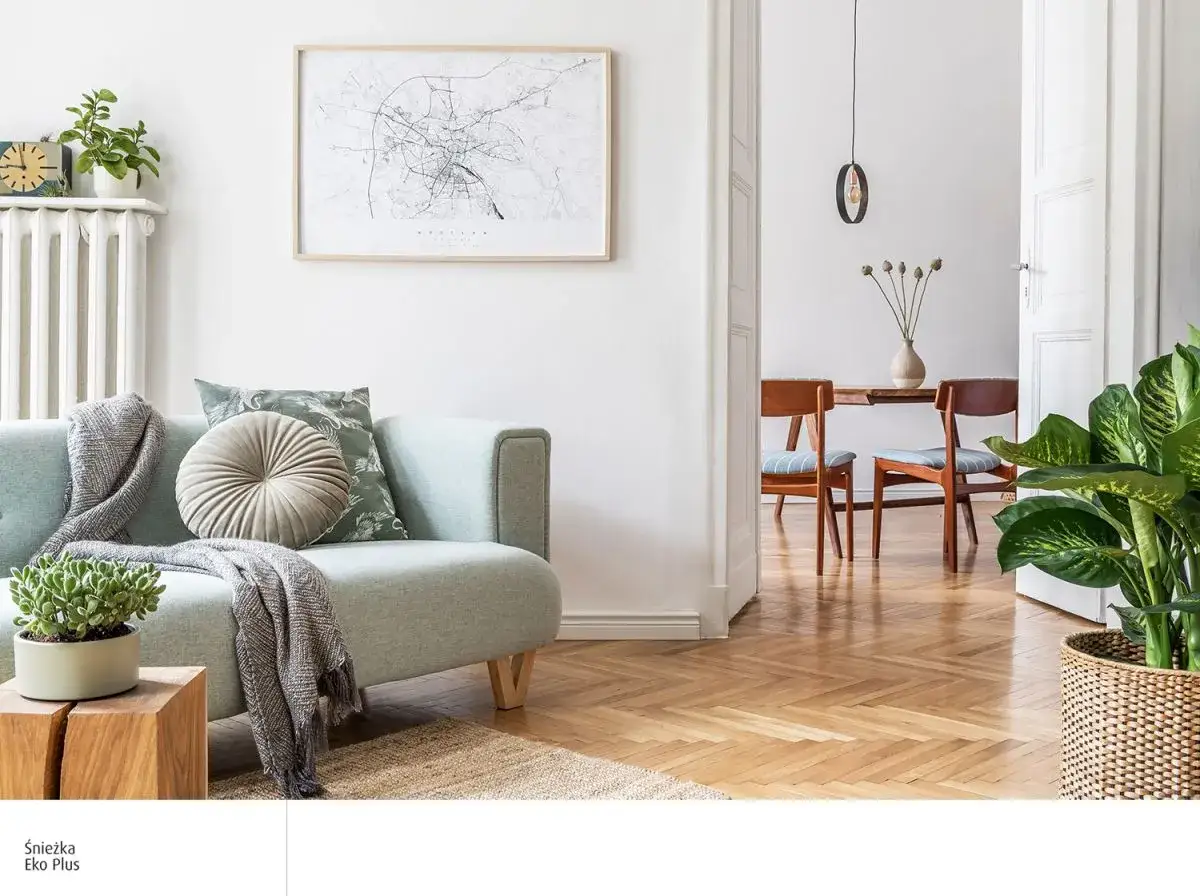 Jasny salon z miętową kanapą, ozdobiony poduszkami i kocem. W tle widać jadalnię z drewnianymi krzesłami. Dominują **kolory naturalne**.