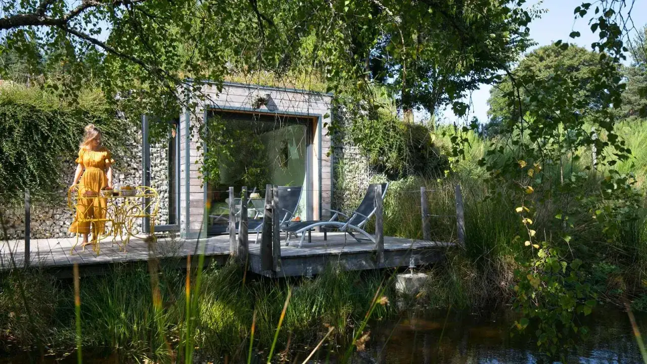 Une femme en robe jaune profite du calme près de sa cabane en Haute-Loire, avec une terrasse en bois et des chaises longues.