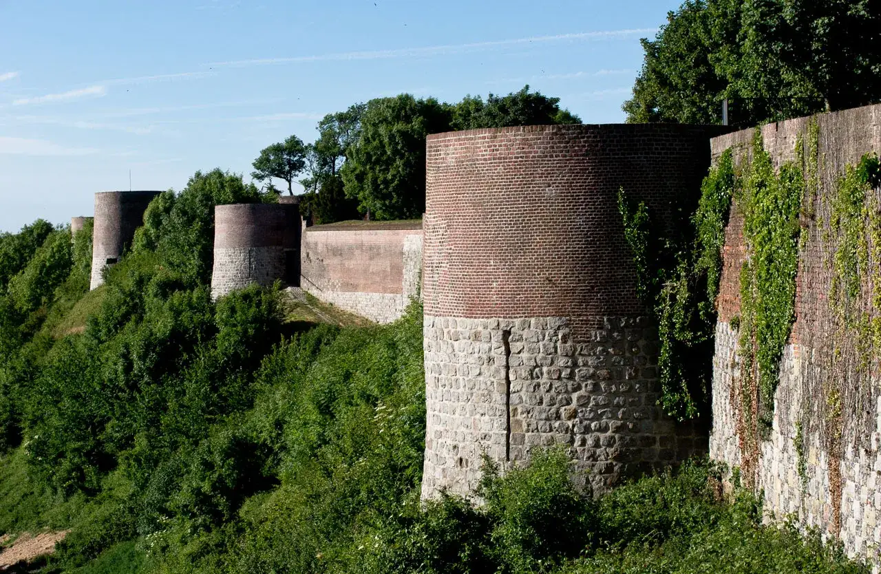 Tours circulaires en briques et pierre du ch&acirc;teau de Montreuil, bord&eacute;es de verdure luxuriante sous un ciel bleu.