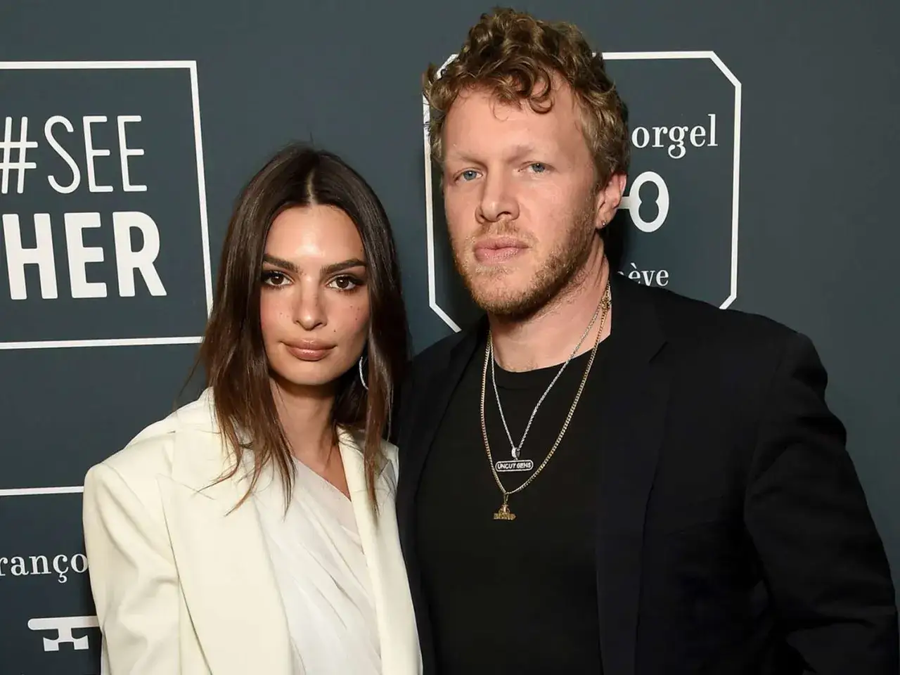 Emily Ratajkowski i Sebastian Bear McClard na ściance. Sebastian nosi naszyjniki, jeden z nich z napisem