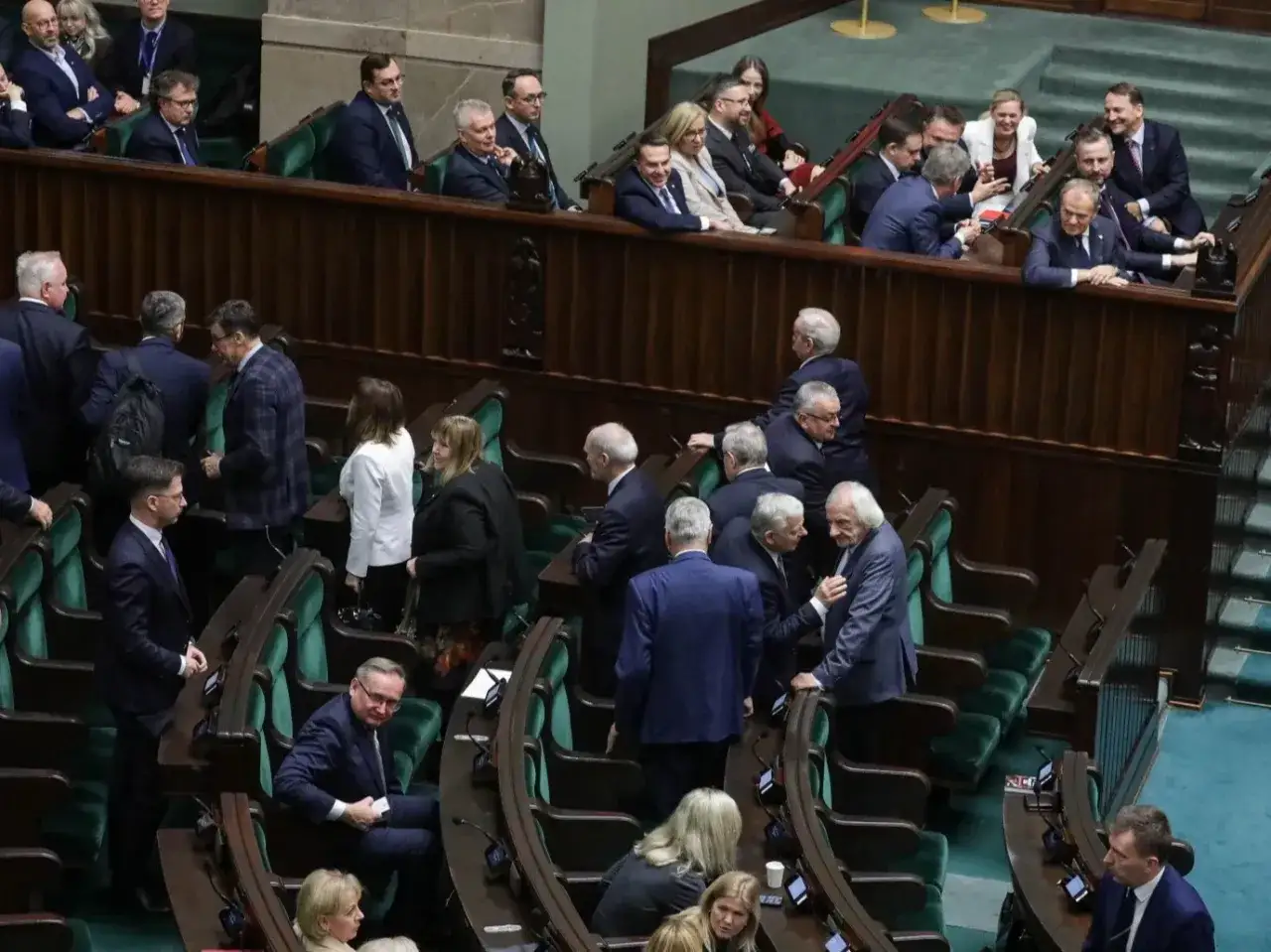 Posłowie w sejmie, dyskutują w ławach. Trudno ocenić, ile jest posłów w sejmie, ale sala jest pełna.