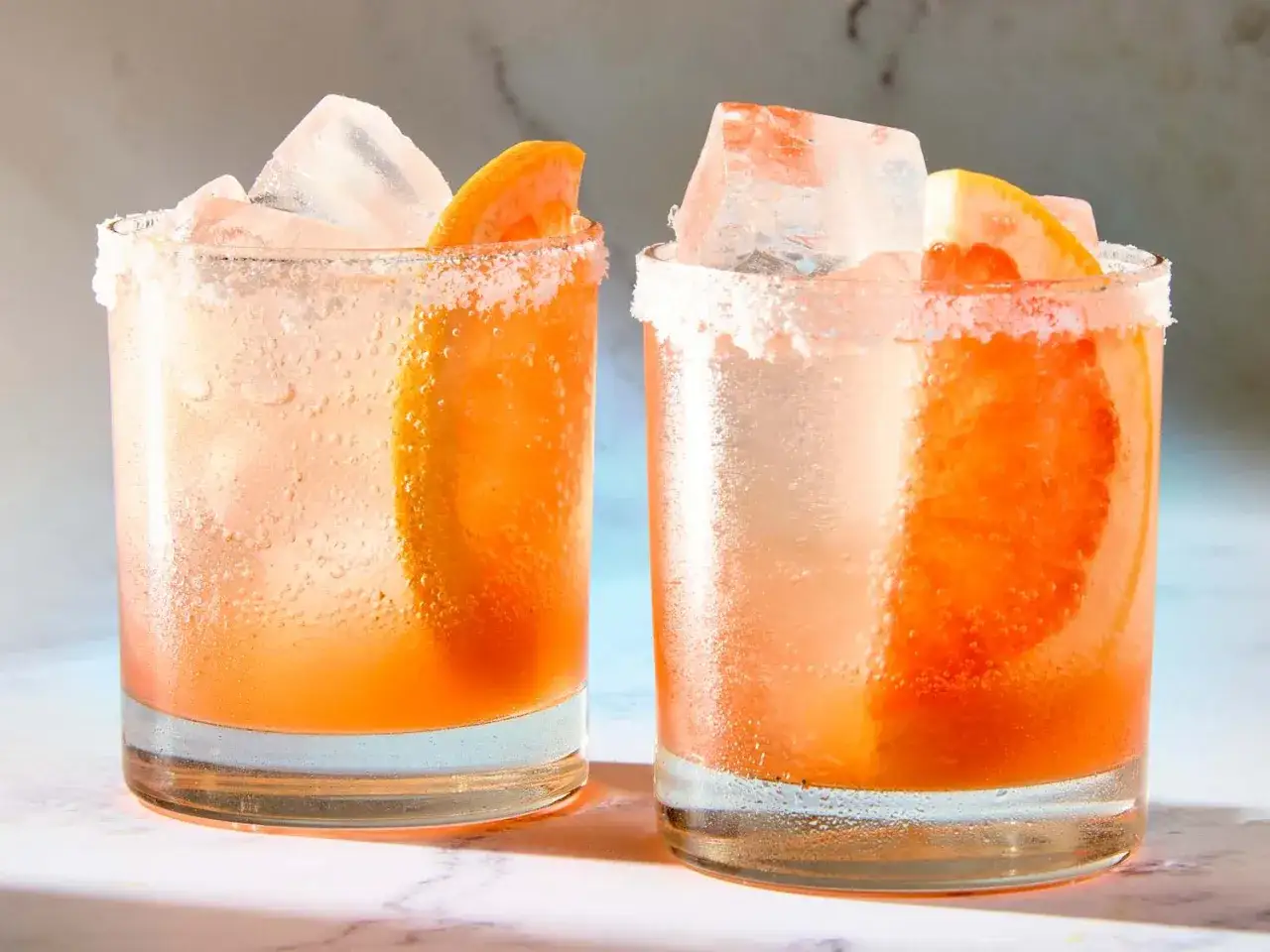 Zwei erfrischende Aperol Paloma Cocktails mit Eis und Grapefruitspalten, die Gläser sind mit Salzrand verziert.