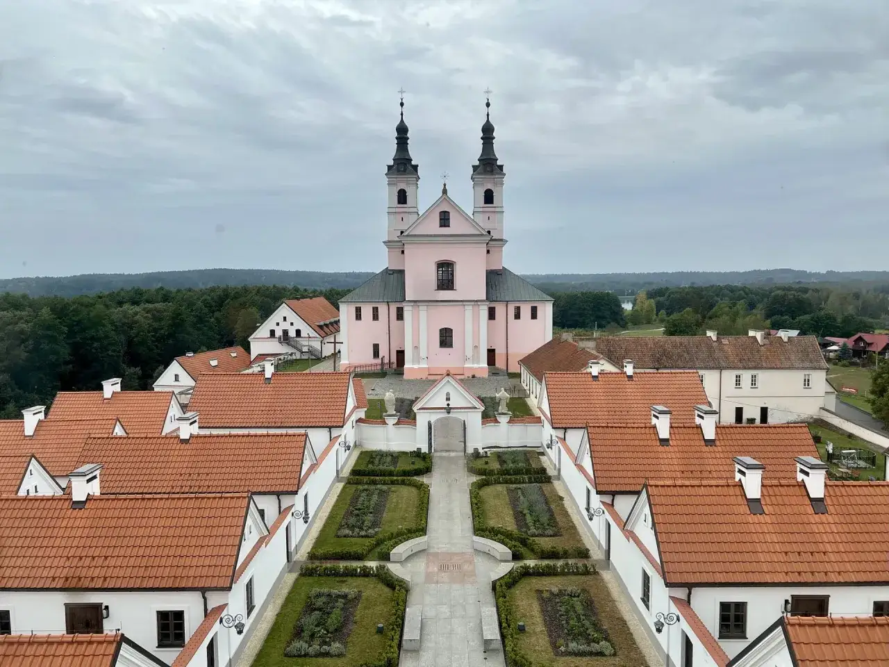 R&oacute;żowy kości&oacute;ł z dwiema wieżami i dziedzińcem z klombami, otoczony zabudowaniami. Piękny widok w okolicy Wigierskiego Parku Narodowego.