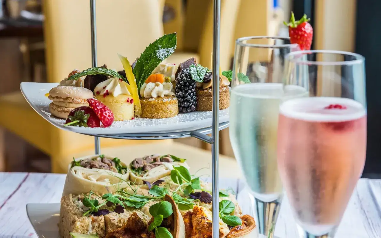 Eleganckie ciastka i makaroniki na piętrowej tacy, idealne do picia prosecco. Obok dwa kieliszki musującego wina.