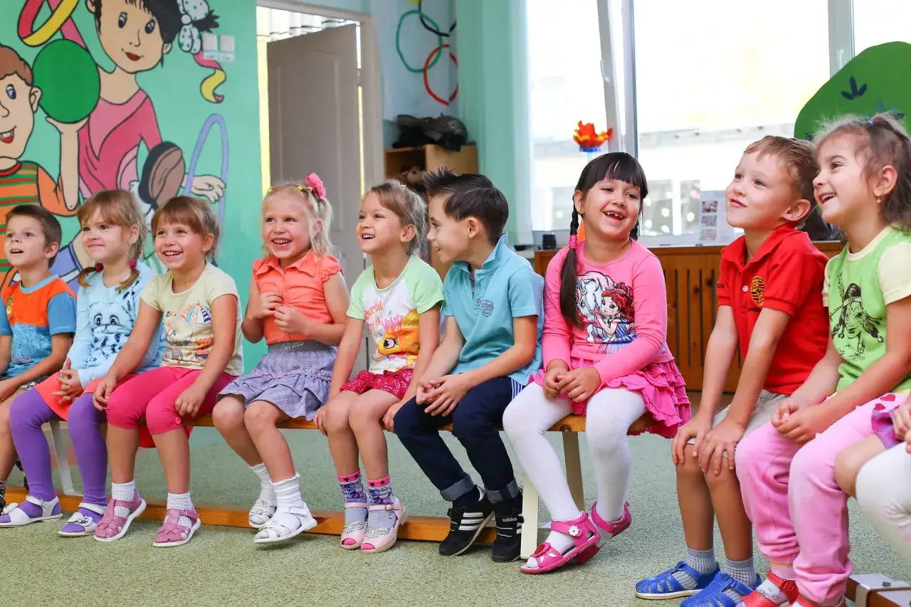 Uśmiechnięte dzieci siedzą w przedszkolu. Nawet nadpobudliwe dziecko w przedszkolu potrafi się cieszyć.
