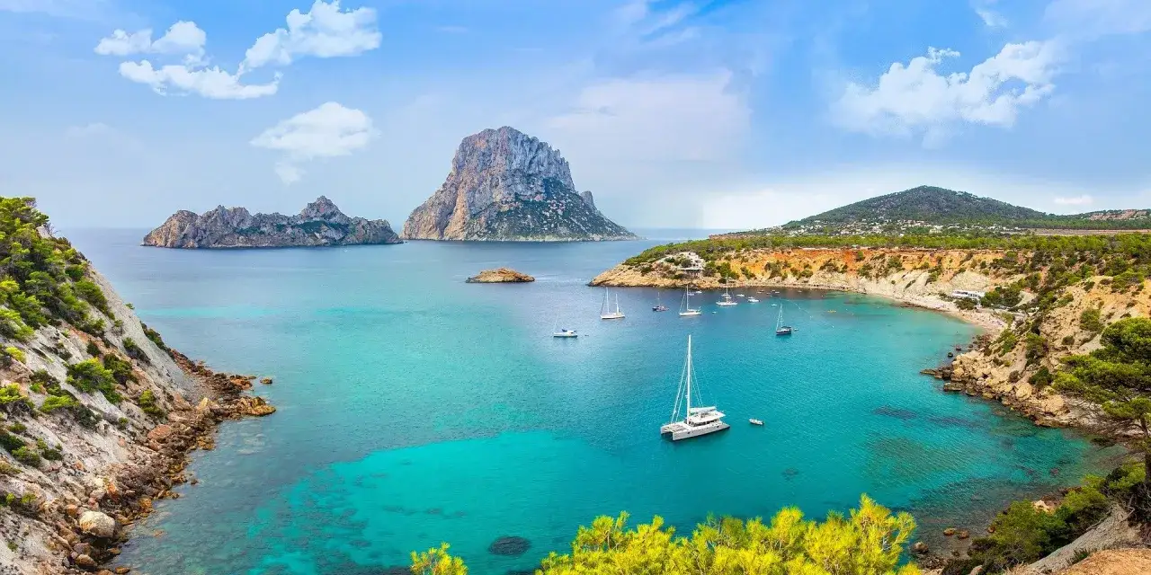 Bah&iacute;a turquesa con veleros y la silueta de Es Vedr&agrave;. Ideas de qu&eacute; ver en Ibiza en 4 d&iacute;as.
