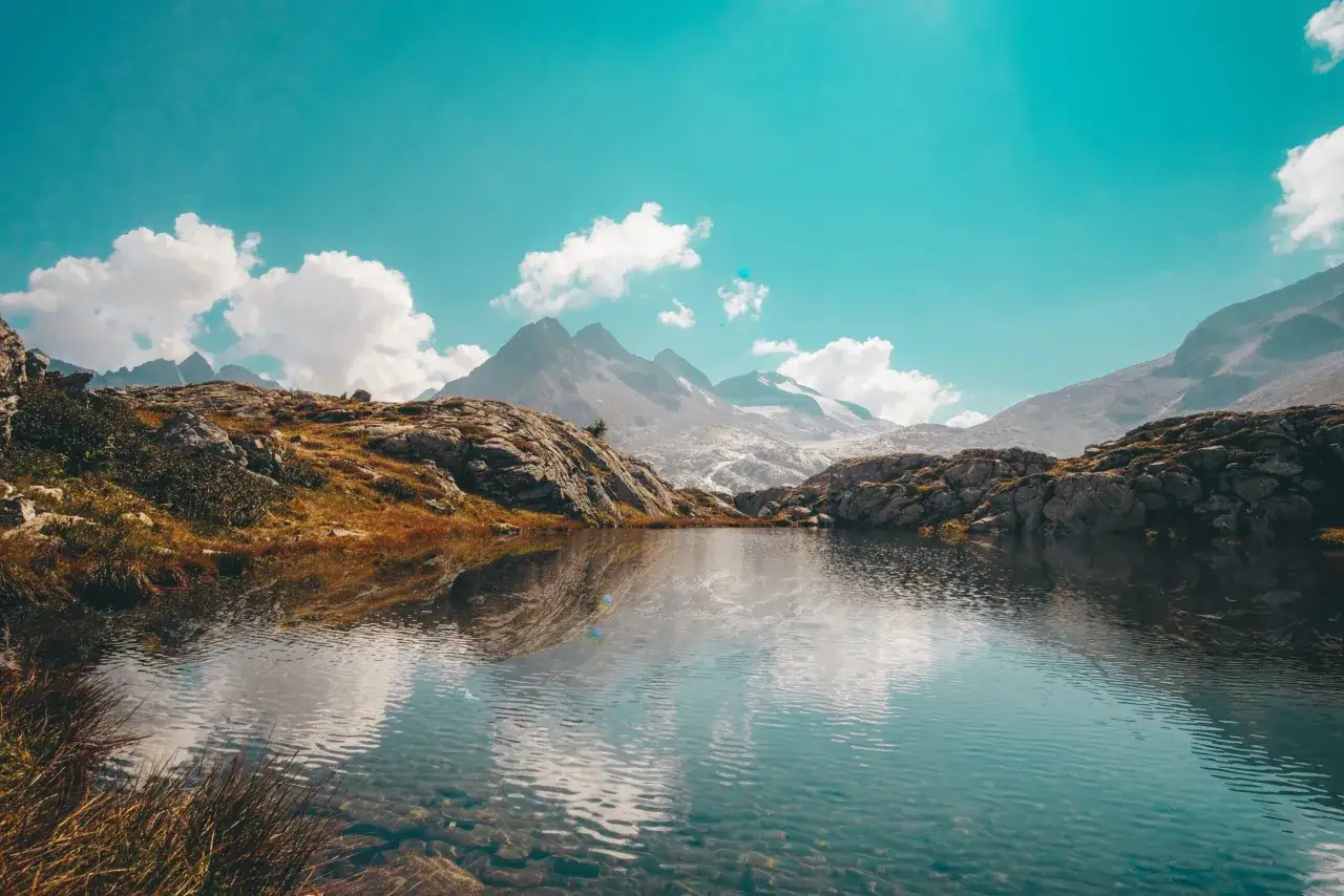 Lago alpino con riflessi di montagne innevate e cielo azzurro, un paesaggio mozzafiato che ricorda il Val di Sole.
