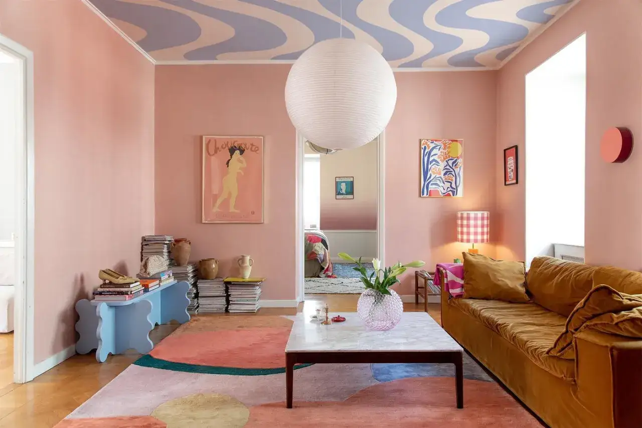 Ett vardagsrum med pastell inredning. Rosa v&auml;ggar, en v&aring;gig lila och ljusbl&aring; takm&aring;lning, en gul soffa och en f&auml;rgglad matta.