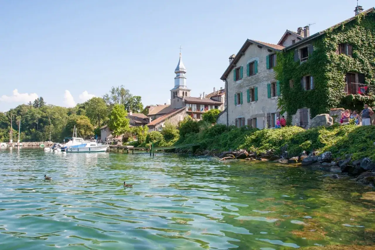 Bateaux amarr&eacute;s, maisons fleuries et clocher se refl&eacute;tant dans l'eau turquoise. Parfaites vacances Alpes &eacute;t&eacute;.