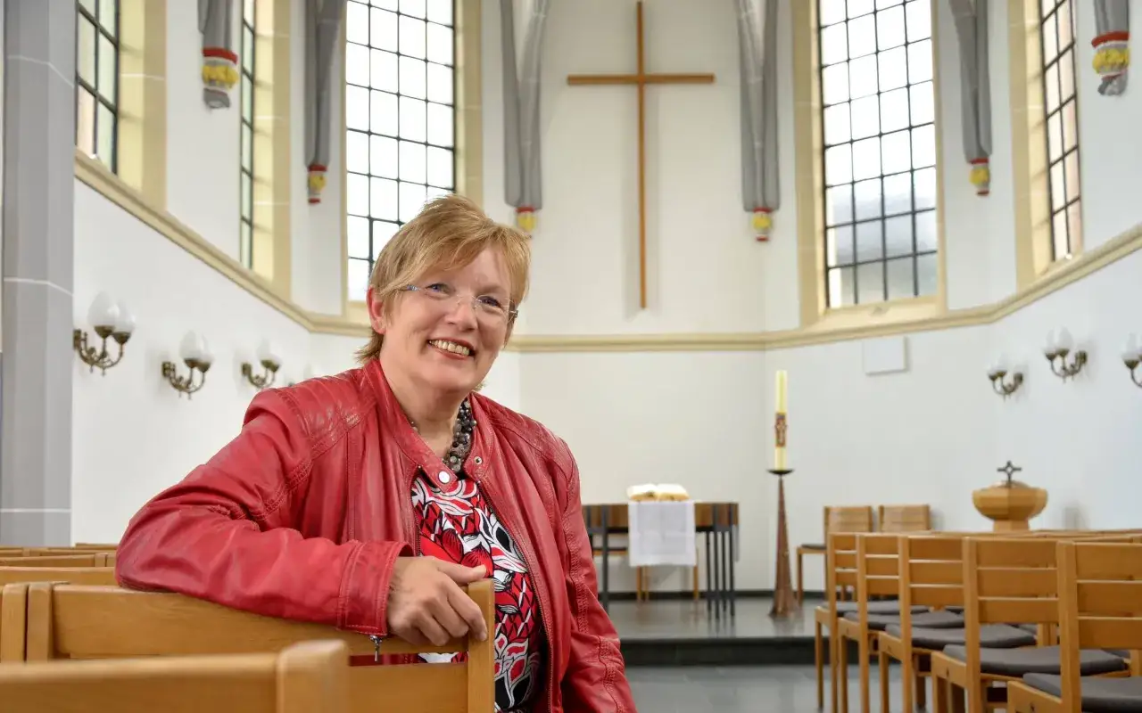L&auml;chelnde Frau in roter Lederjacke sitzt in Kirche. Ein sch&ouml;nes Bild f&uuml;r den Pfingstmontag Feiertag.