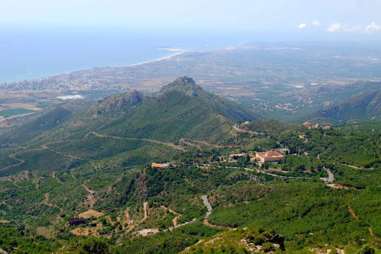 Vista panorámica del **Desert de les Palmes**, con el mar Mediterráneo al fondo y edificios históricos entre la vegetación.