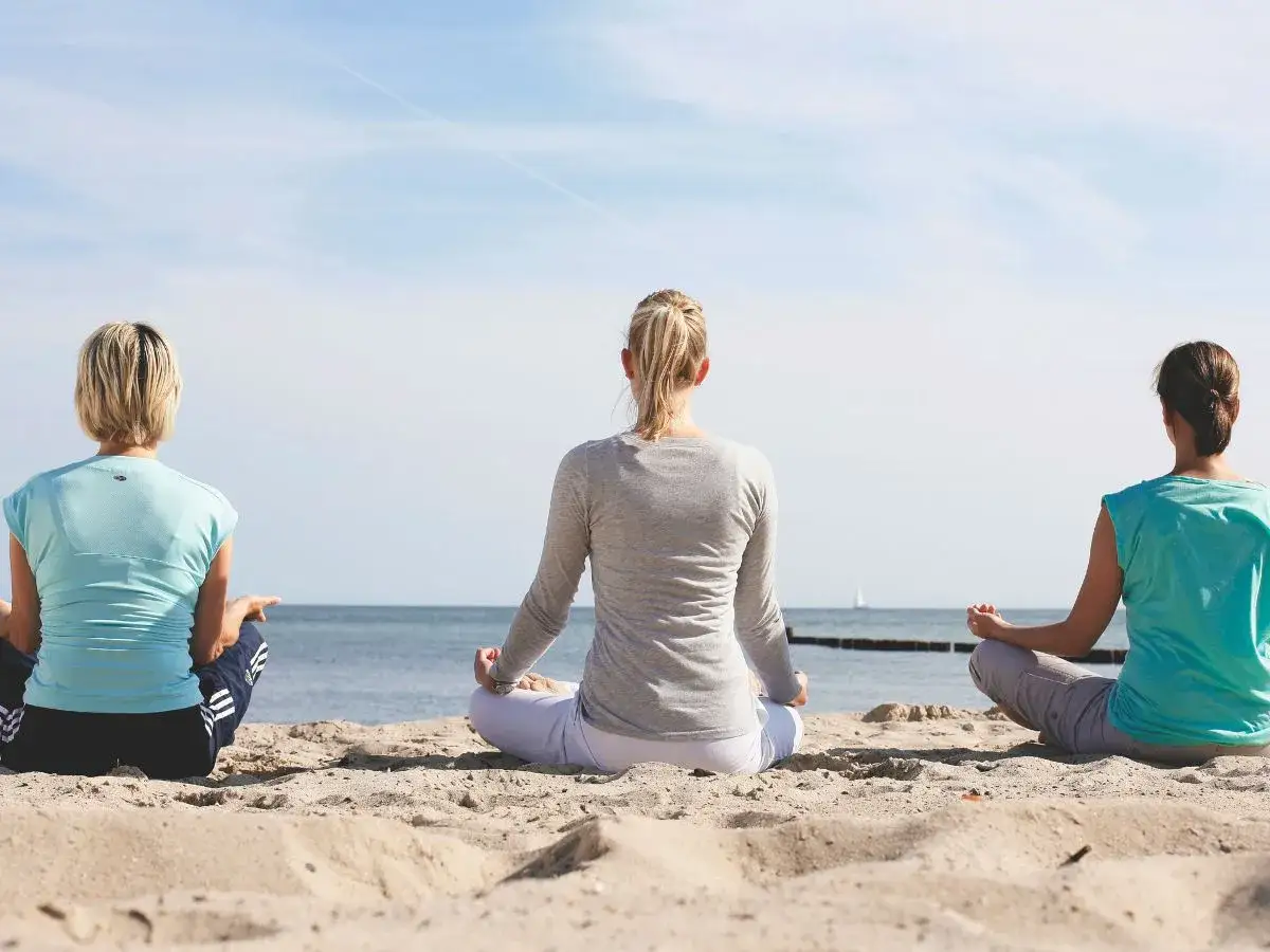 Drei Frauen meditieren am Strand. Die frische Meeresluft tut gut bei einer Asthma Kur am Meer.