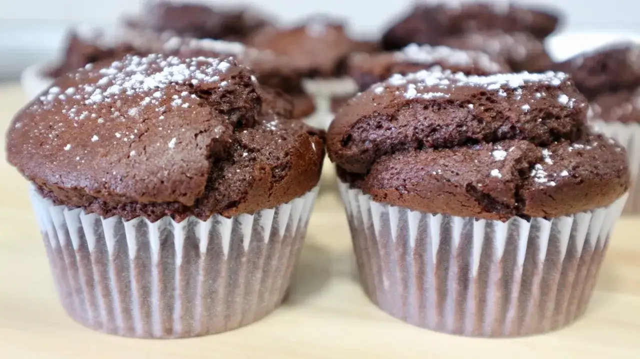 Dos magdalenas de chocolate esponjosas, espolvoreadas con azúcar glas, listas para disfrutar.
