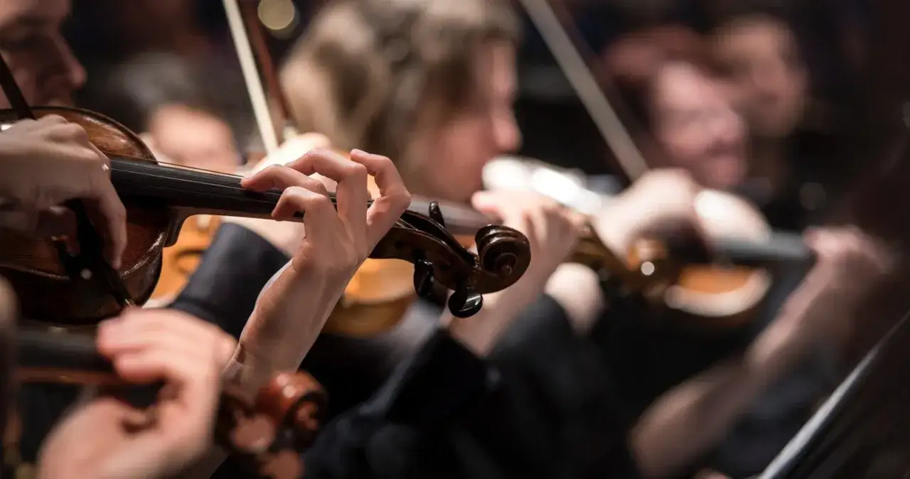 H&auml;nde spielen Geigen, w&auml;hrend dramatische Musik Klassiker erklingen. Ein Orchester in Aktion.