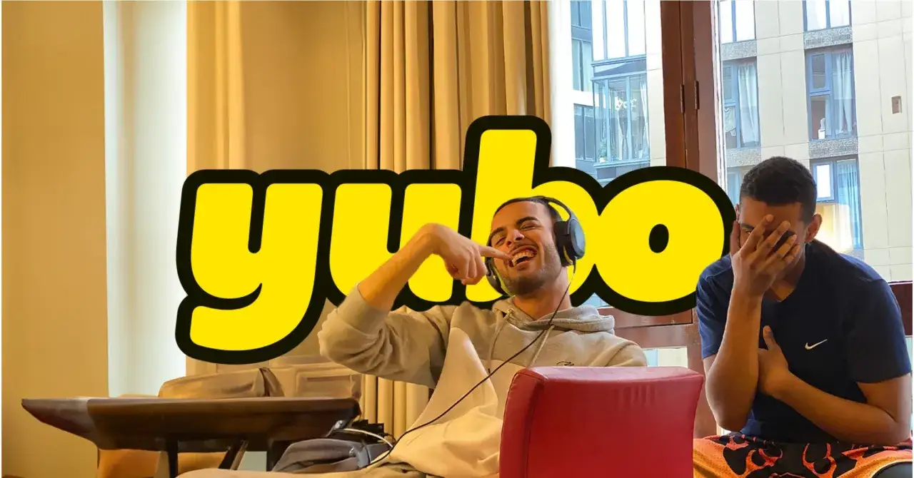 Dwóch młodych mężczyzn śmieje się, jeden z nich wskazuje palcem na zęby. Nad nimi wielki napis 
