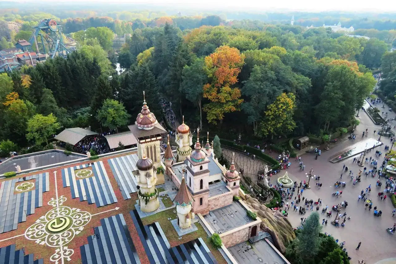 A fairytale castle with ornate domes and towers, surrounded by lush trees and a bustling theme park. A perfect day trip from Amsterdam to Efteling!