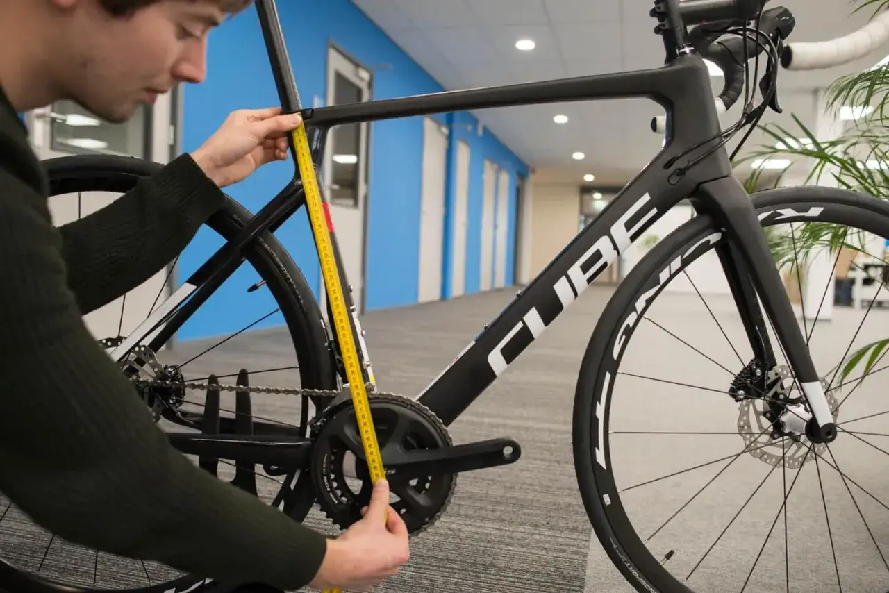 Man meet de **cube framemaat** met een gele meetlint. De fiets is zwart met witte letters.