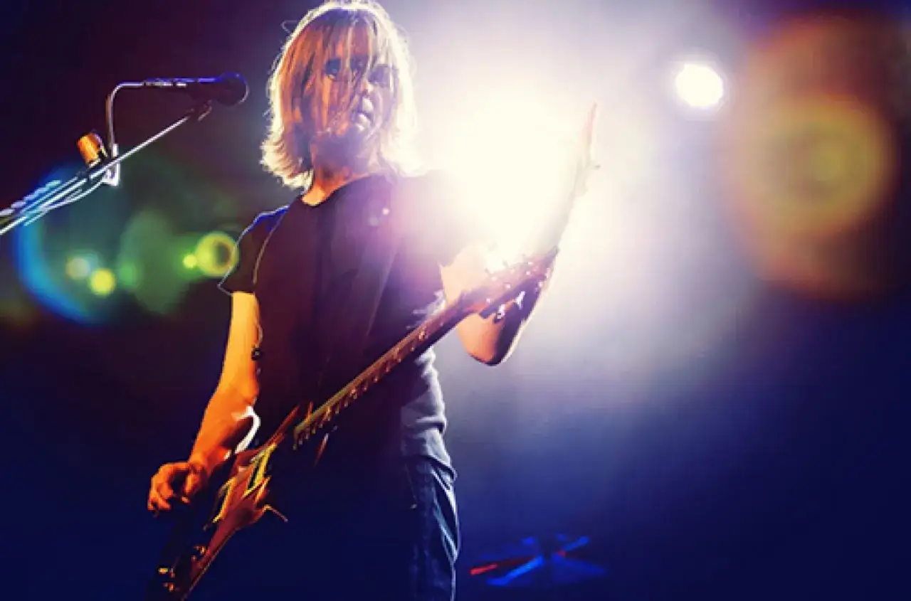 Steven Wilson z zespołem na scenie, grający na gitarze elektrycznej w blasku reflektorów.
