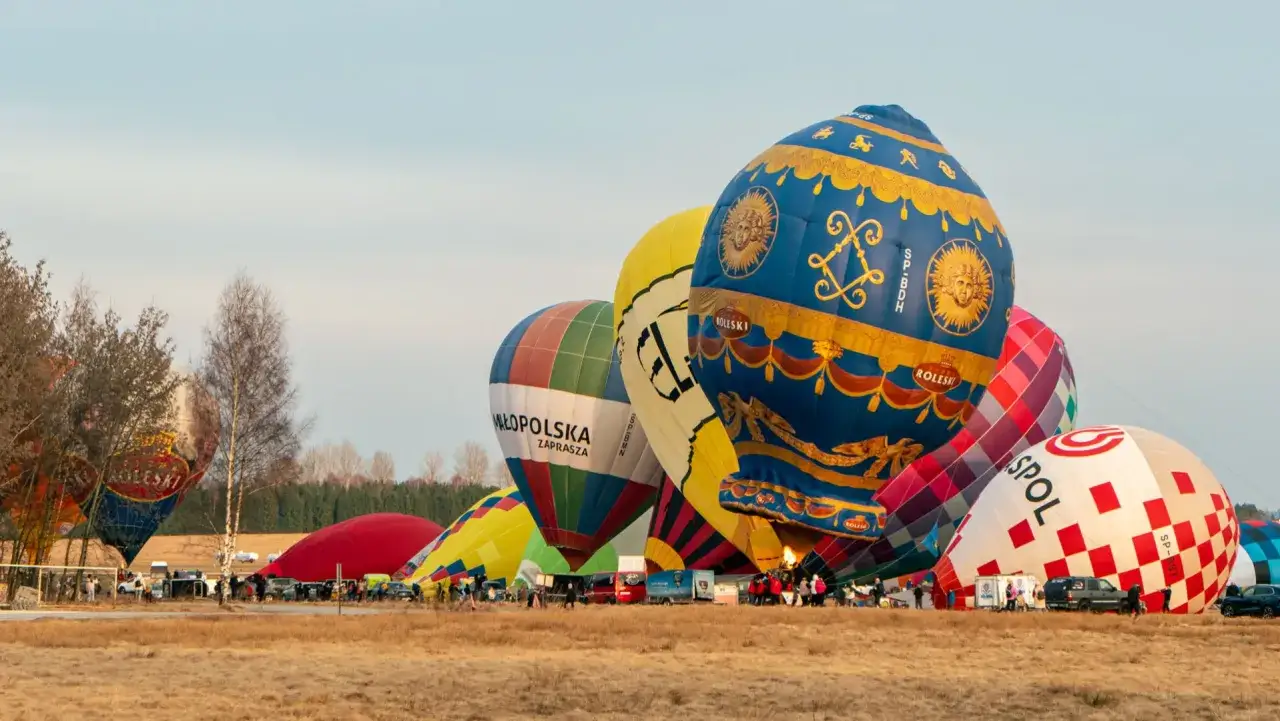 Kolorowe balony, w tym niebieski z motywem słońca i złote zdobienia, przygotowują się do startu w Nowym Targu.