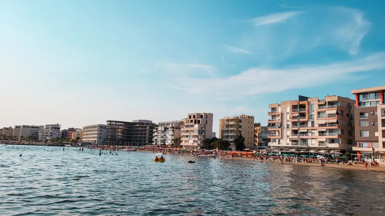 Słoneczna plaża w Durr&euml;s tętni życiem. Ludzie kąpią się w morzu, opalają pod parasolami i spacerują wzdłuż brzegu.