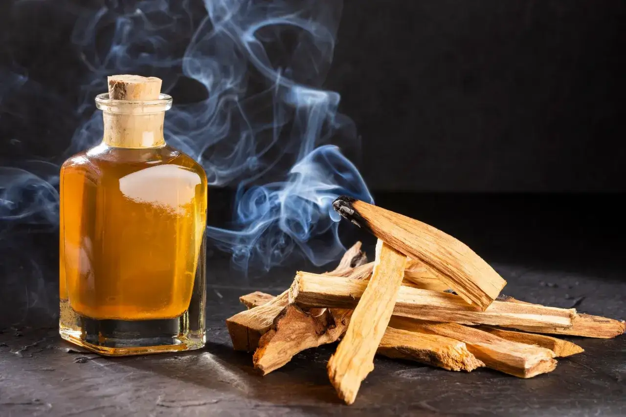 Botella de aceite dorado y astillas de palo santo humeante, elementos para un ritual de limpieza energ&eacute;tica.