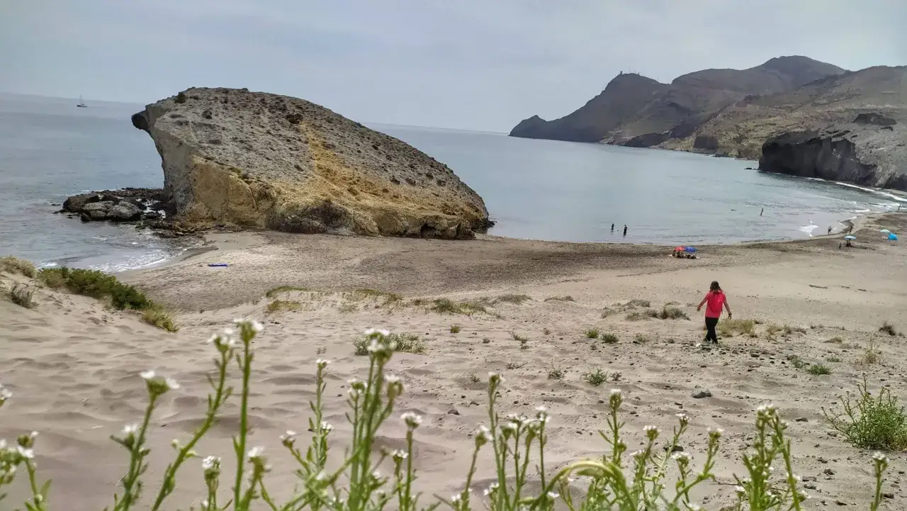 Una persona camina por la arena dorada de la playa de Mónsul, con formaciones rocosas imponentes y el mar azul de fondo.
