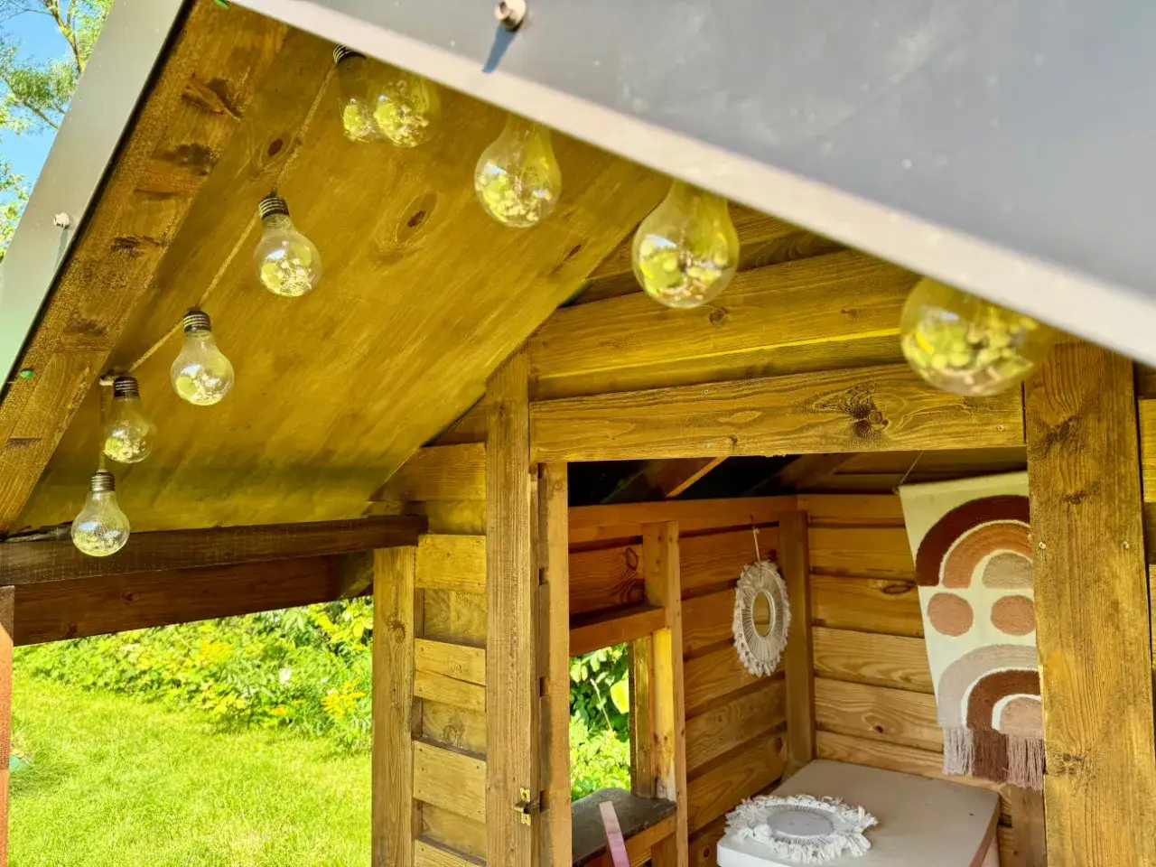 Jak ozdobić domek dla dzieci? Girlanda z żarówek i boho dekoracje nadają mu przytulny klimat.