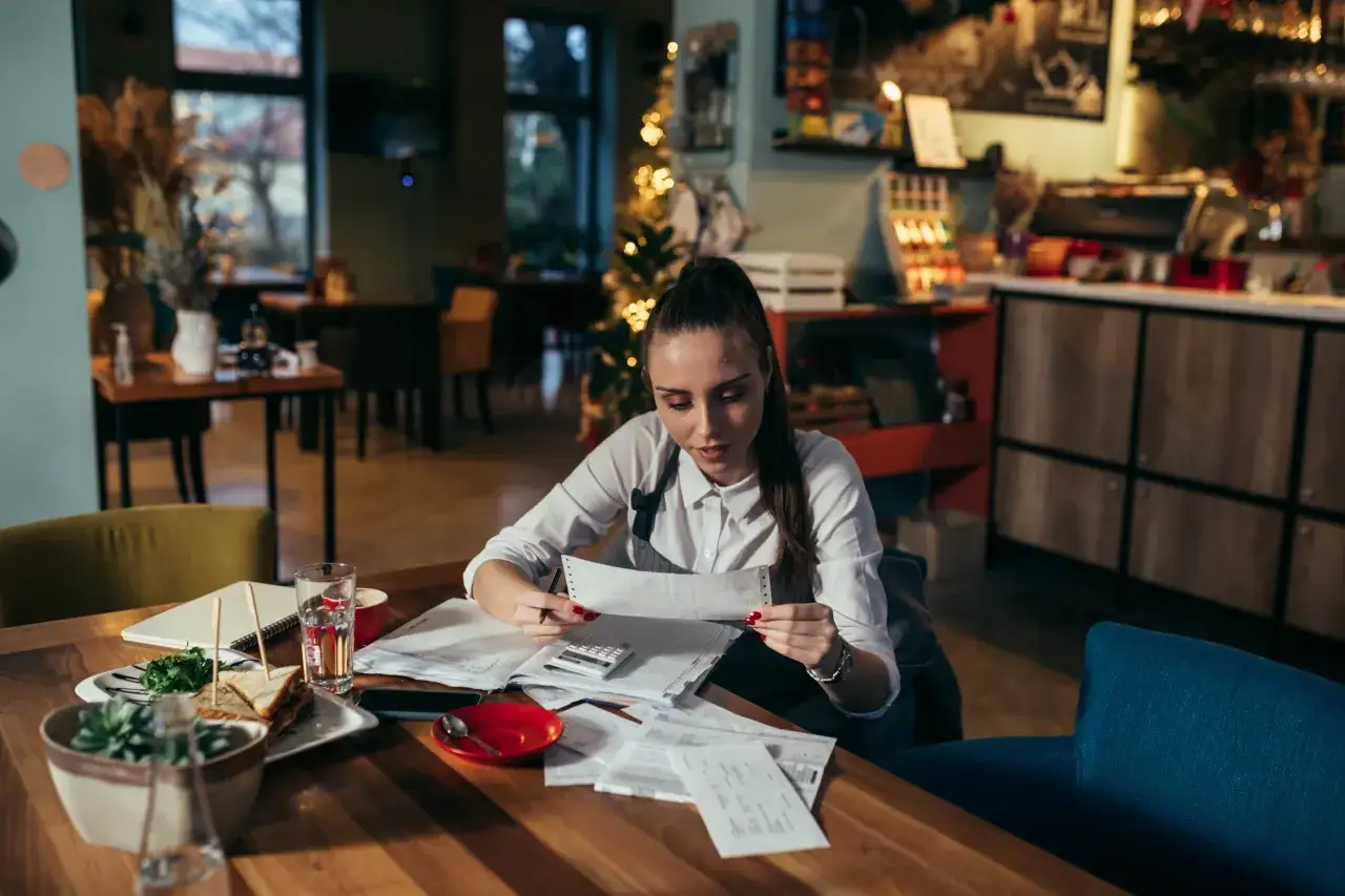 Mujer revisa facturas en un restaurante, calculando cu&aacute;nto cobra Glovo a los restaurantes.