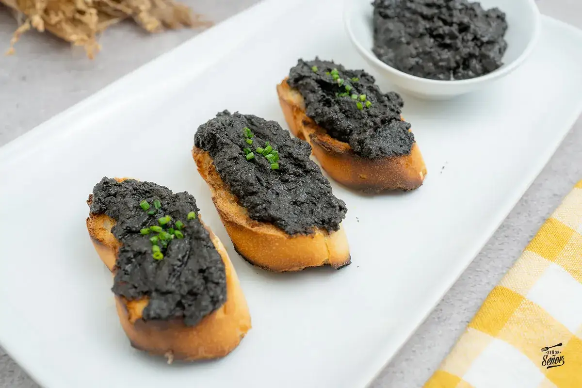 Tostadas con paté de aceitunas negras, perfectas para tus recetas con aceitunas negras. Decoradas con cebollino fresco.