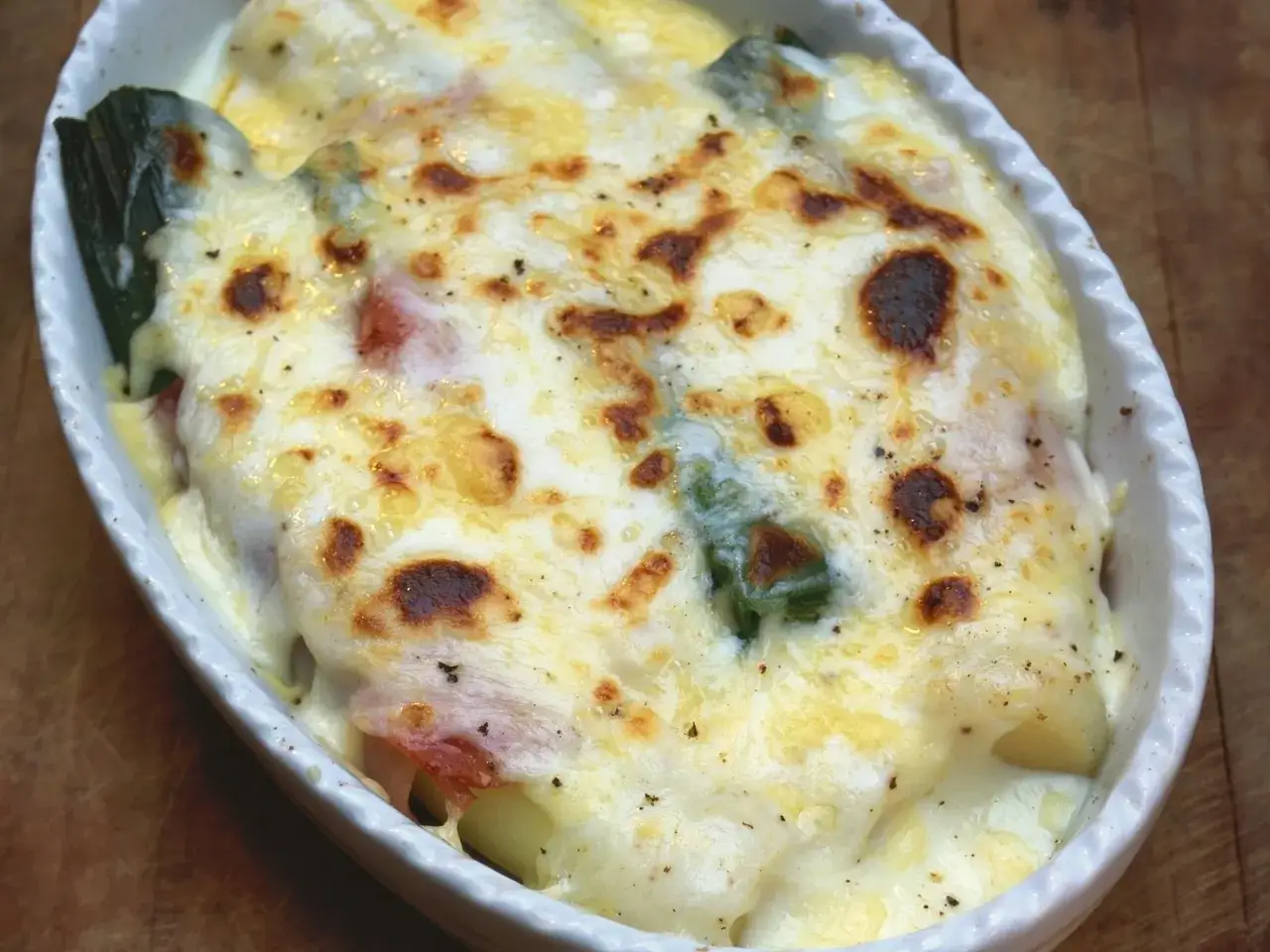 Herzhaft überbackener Lauch mit Schinken und geschmolzenem Käse in einer weißen Auflaufform.