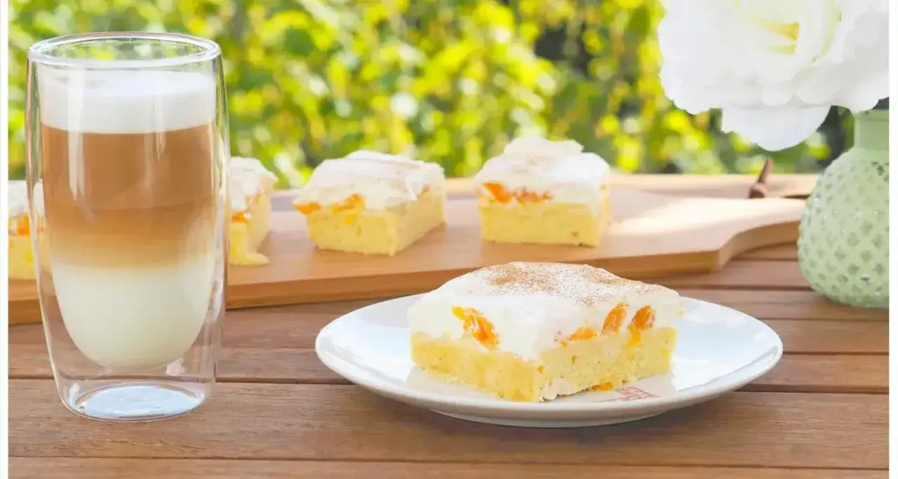 Ein Stück bester Mandarinen Quark Kuchen mit Sahne und Zimt, daneben ein Latte Macchiato.