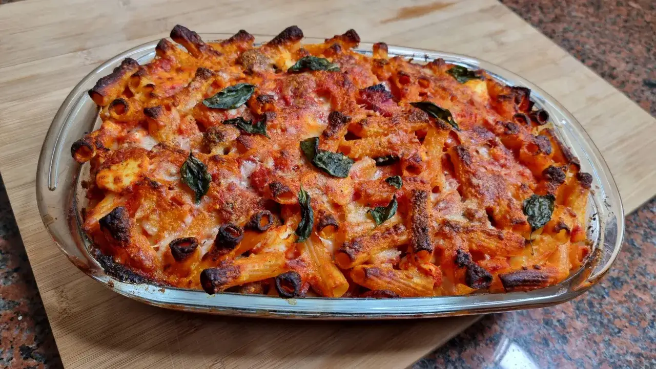 Un invitante piatto di pasta al forno napoletana, con pasta rigata dorata, sugo rosso e formaggio filante, guarnito con foglie di basilico fresco.