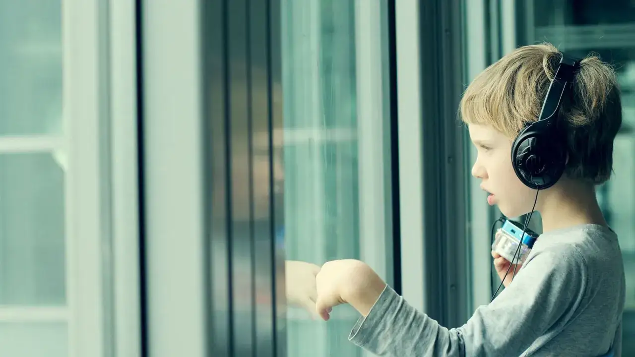 Junge mit Kopfh&ouml;rern und MP3-Player blickt nachdenklich aus dem Fenster. Seine Reizoffenheit bei Kindern zeigt sich in seiner Konzentration auf die Welt drau&szlig;en.