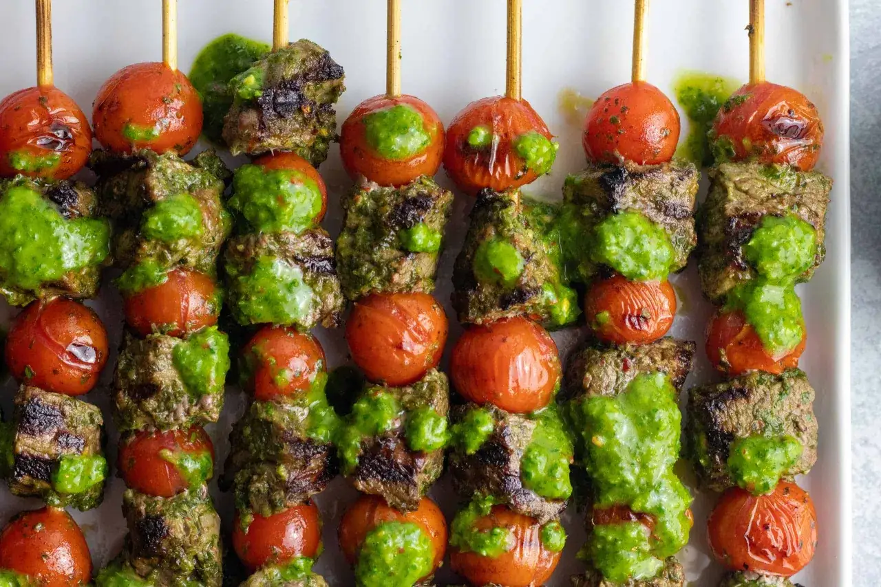 Grillspett med saftigt kött och körsbärstomater, generöst täckta med en grön sås. En perfekt italiensk grill-upplevelse.