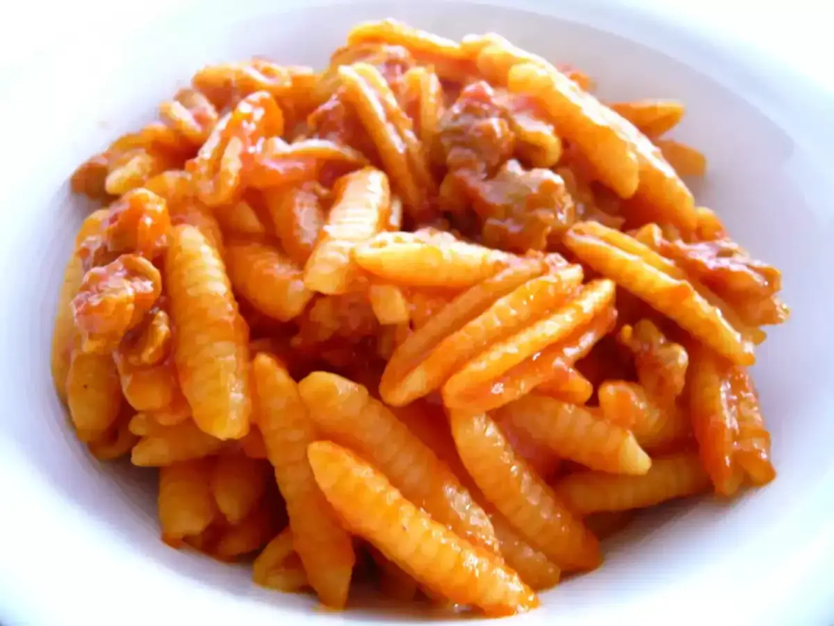 Malloreddus alla campidanese, pasta sarda con sugo di pomodoro e salsiccia, serviti in un piatto bianco.