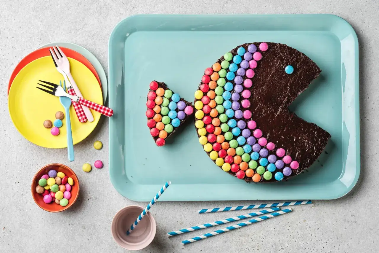 G&acirc;teau en forme de poisson color&eacute;, parfait pour un enfant. Il est d&eacute;cor&eacute; de bonbons multicolores formant un arc-en-ciel.