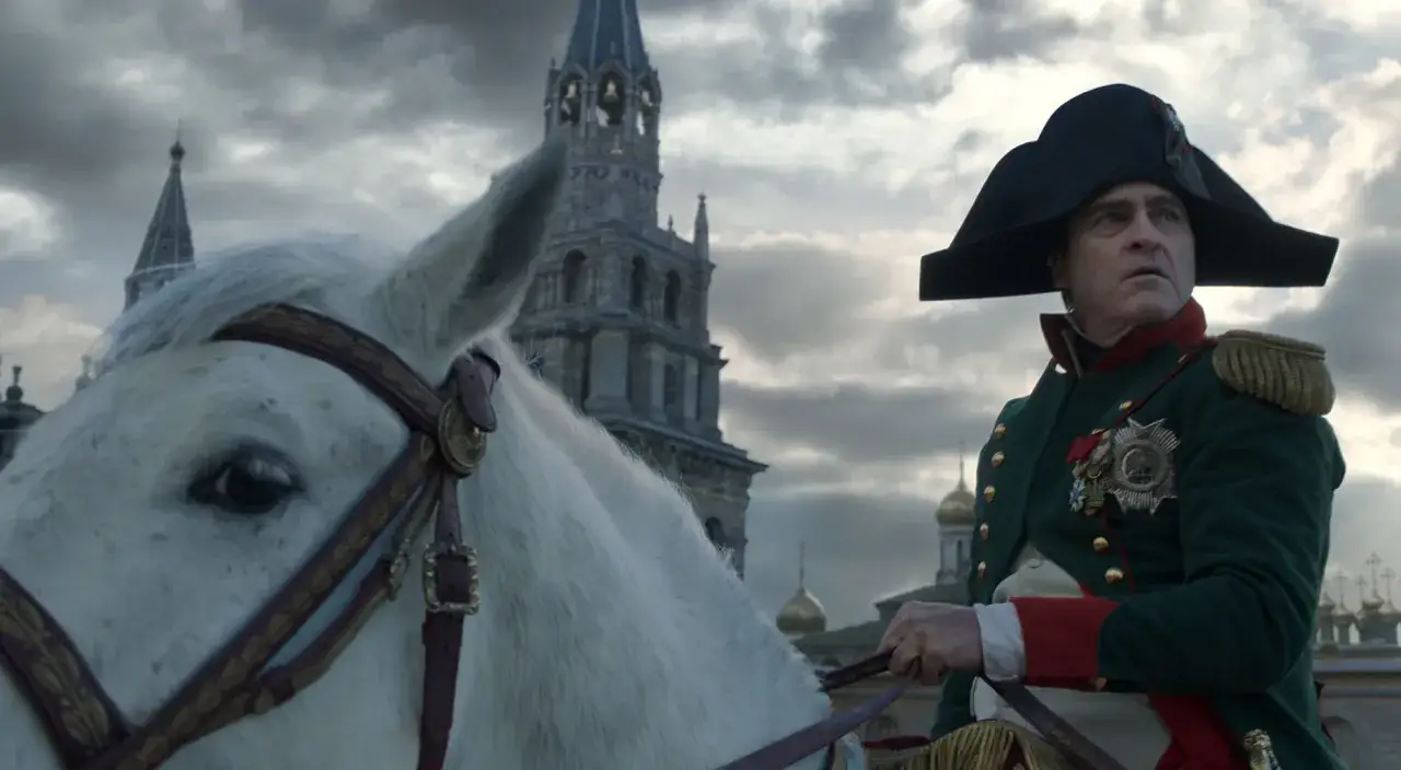 Joaquin Phoenix jako Napoleon w filmie. Recenzja filmu ukazuje go na białym koniu przed cerkwią.