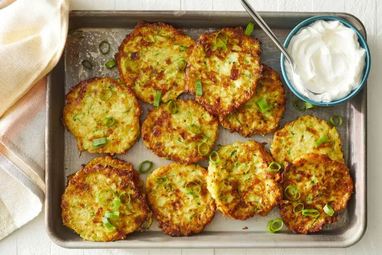 Gyllene, krispiga zucchiniplättar toppade med salladslök, serverade på en plåt med en skål gräddfil. Ett perfekt zucchini recept för en lätt måltid.