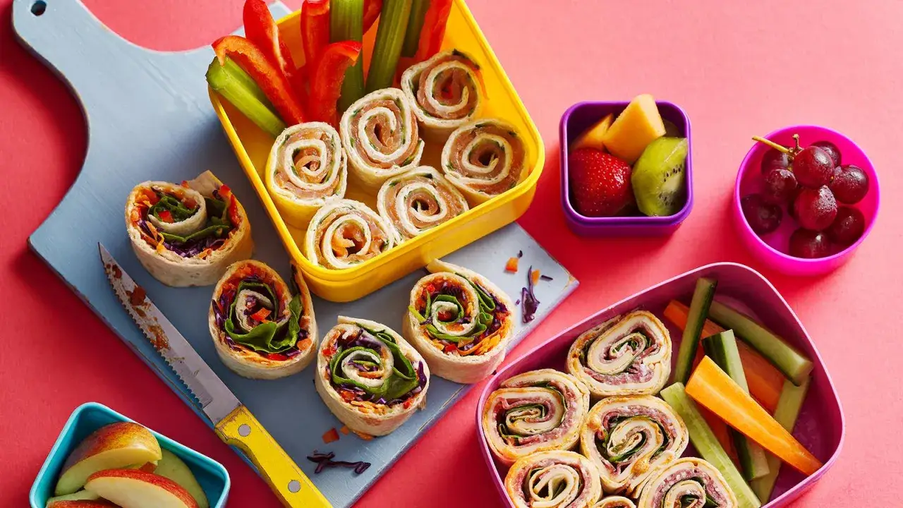 Bunte Wraps zum Mitnehmen, gef&uuml;llt mit Lachs oder Gem&uuml;se, neben Obst und Gem&uuml;sesticks. Perfekt f&uuml;r unterwegs!